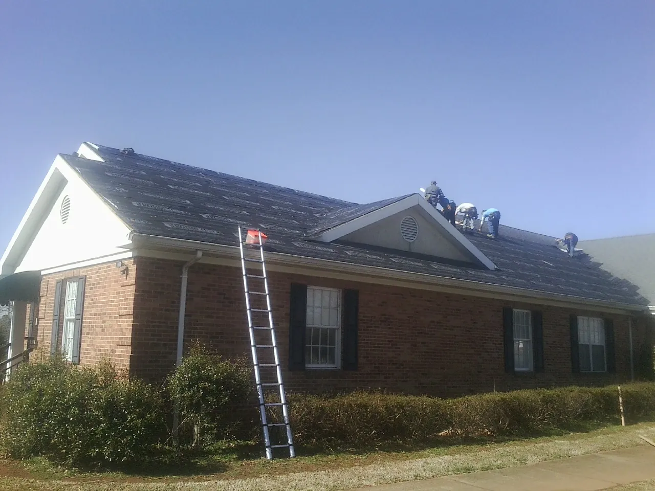 Crew tearing shingles off a brick ranch roof with a ladder set — Emergency Roof Repair work by our crew in Jamesport