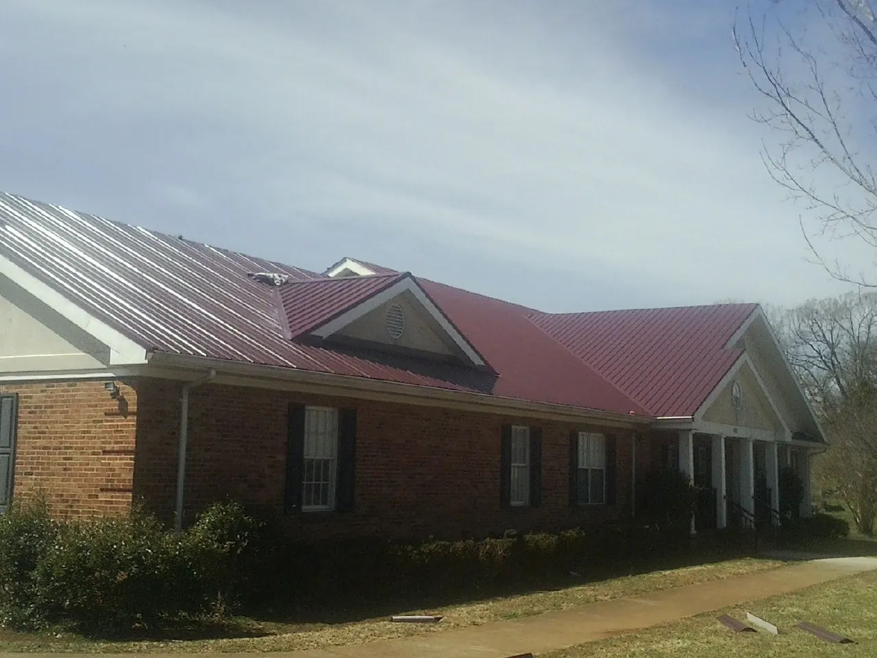 Red metal roof with gabled entries on a long brick building, from a Hail Damage Roof Repair job in Jamesport