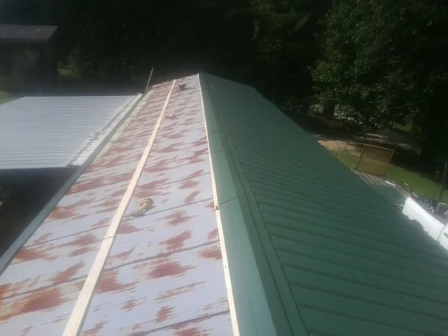 Old rusted panels beside newly installed green metal roofing — Wind Damage Roof Repair by Roofing Brothers in Jamesport