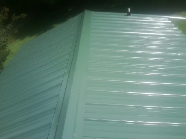 New green metal panels meeting at the ridge of a roof — Flat Roof Repair work by our crew in Jamesport