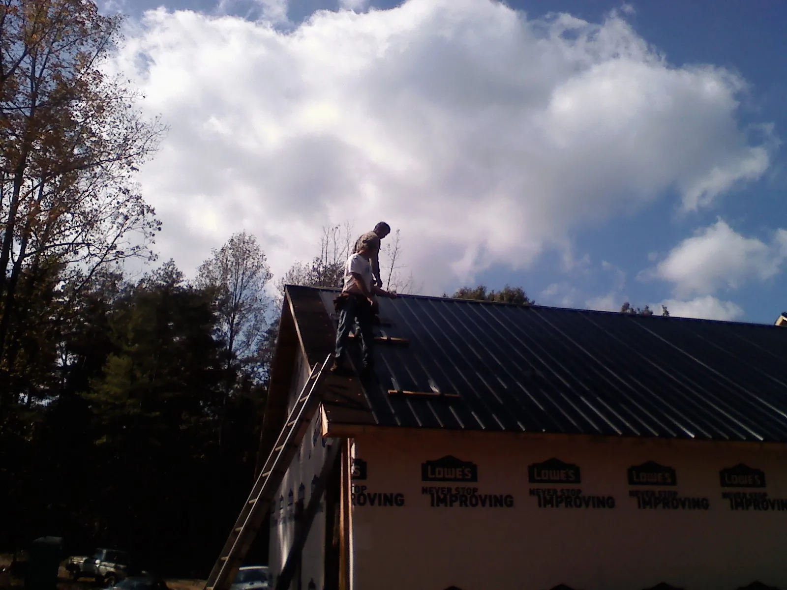Roofer fastening dark metal panels high against a cloudy sky, from a Roof Inspection job in Jamesport