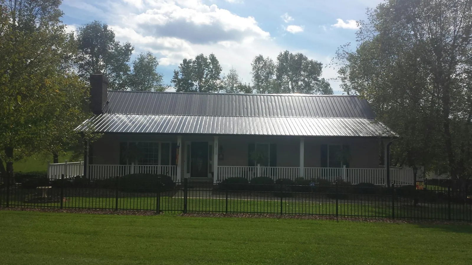 Gray metal roof on a brick ranch with a full width front porch — Gutter Guard Installation work by our crew in Jamesport