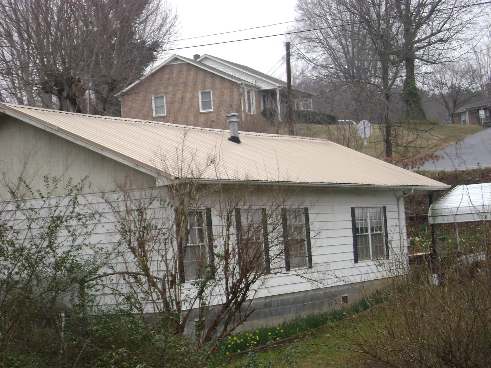 Tan metal roof on a white sided house set into a hillside — Commercial Roofing by Roofing Brothers in Jamesport