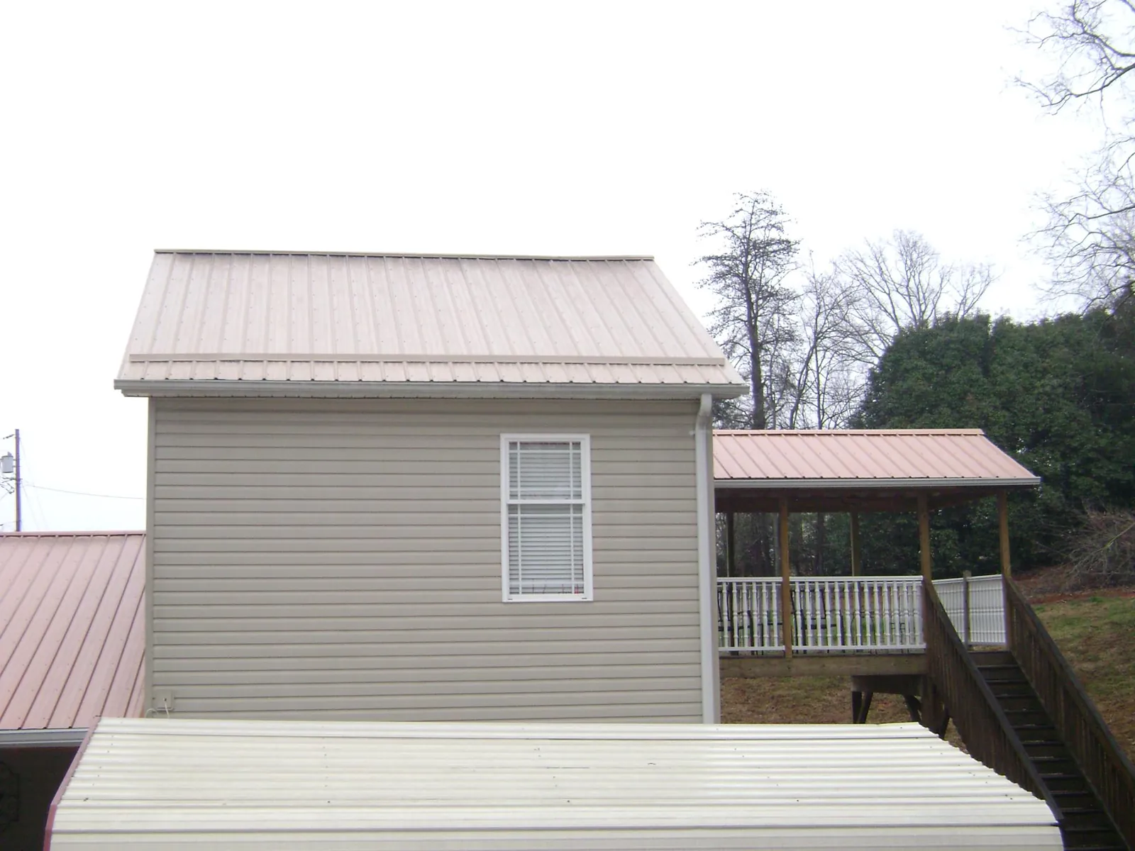 Tan metal roofs on a two story addition and attached porch, from a Roof Replacement job in Jamesport